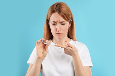 Photo of Upset woman with herpes applying cream on lips against light blue background