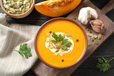 Delicious pumpkin soup in bowl on wooden table, flat lay