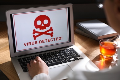 Photo of Woman using laptop with warning about virus attack at workplace, closeup