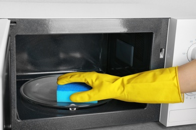 Photo of Woman cleaning microwave oven with sponge, closeup