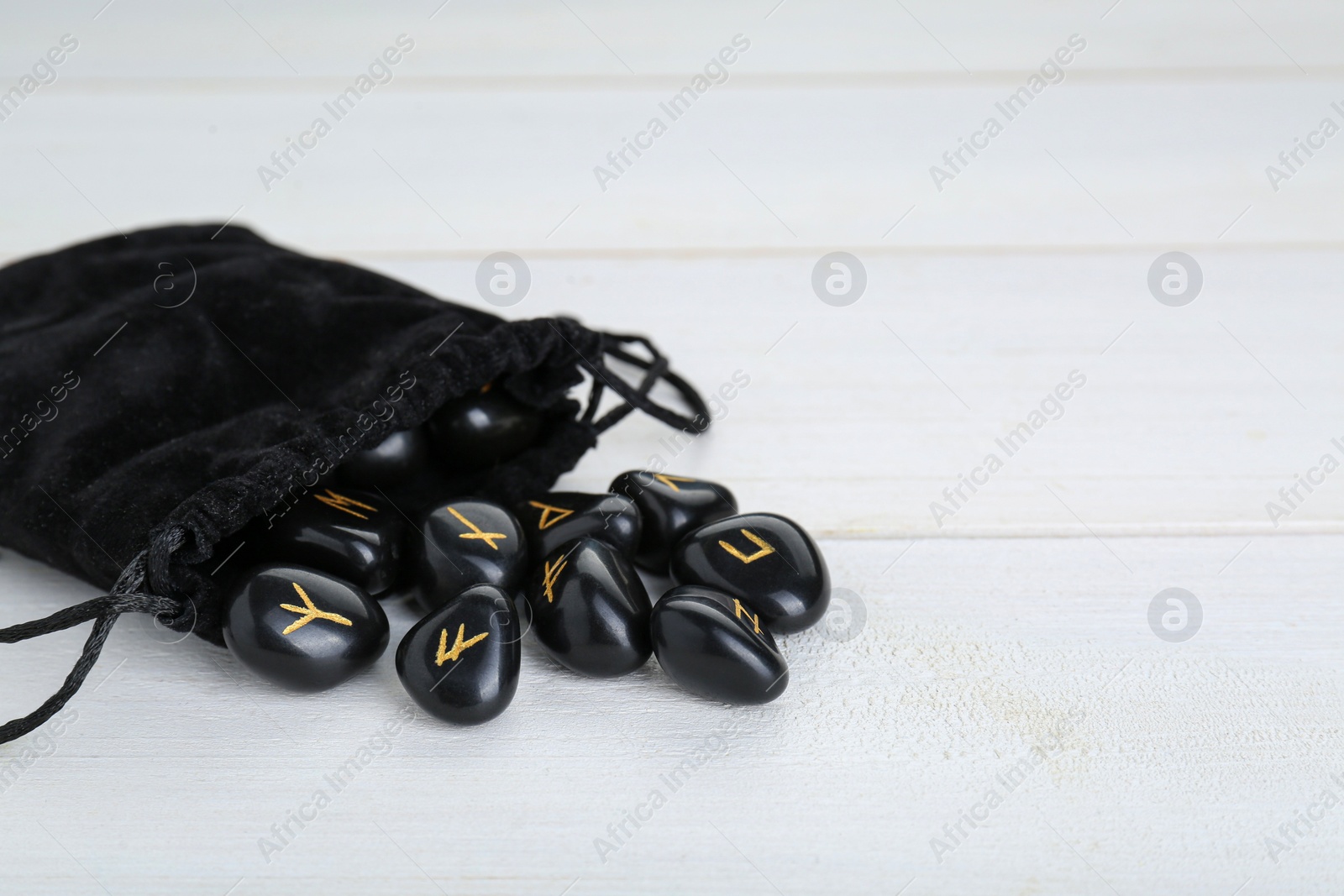 Photo of Bag with black rune stones on white wooden table