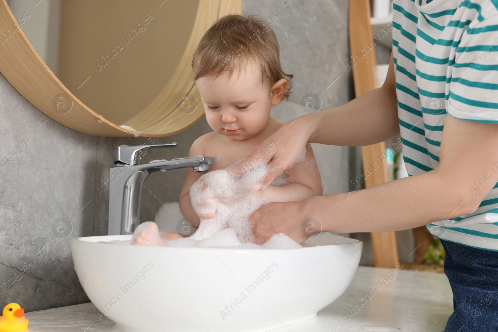 Photo of Mother washing her little baby in sink at home