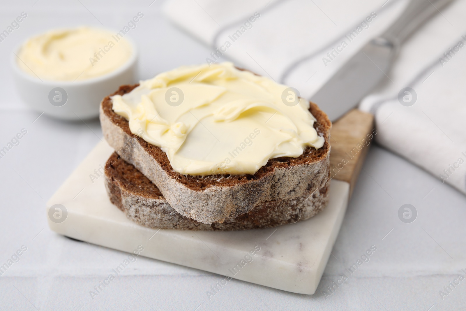 Photo of Slices of tasty bread with butter on white tiled table, closeup