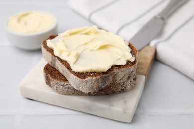 Slices of tasty bread with butter on white tiled table, closeup