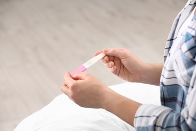 Young woman with pregnancy test at home, closeup. Space for text