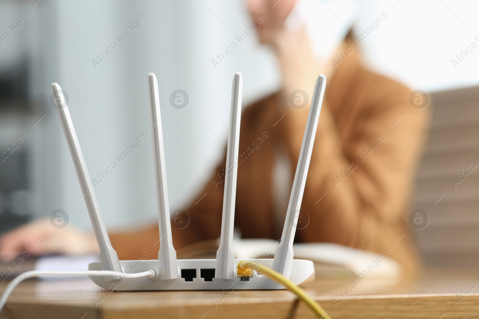 Photo of Woman talking on smartphone at table indoors, focus on Wi-Fi router