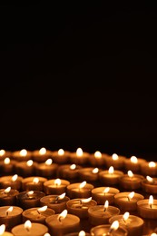 Photo of Burning candles on table against black background, space for text