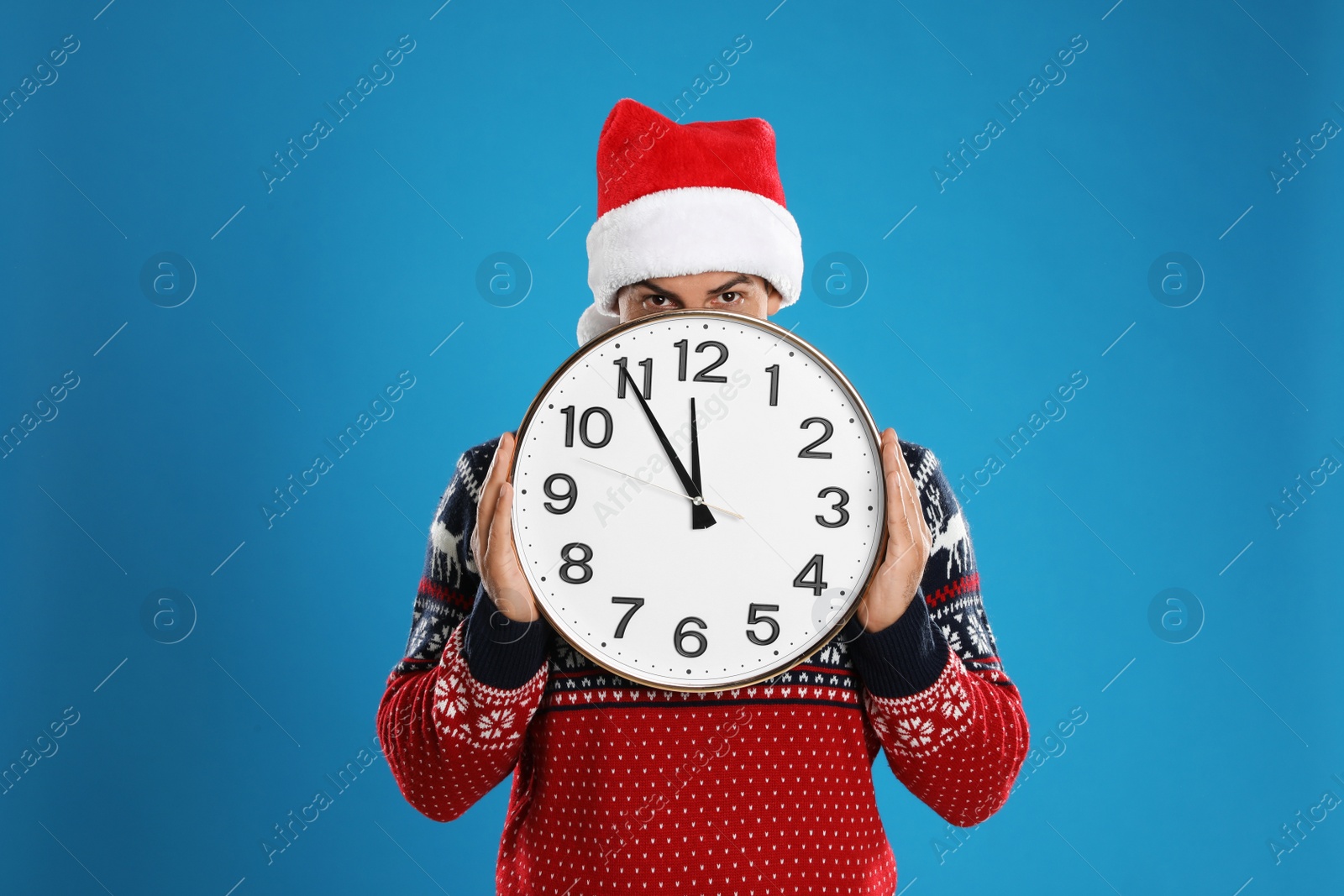 Photo of Man in Santa hat with clock on blue background. New Year countdown