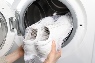 Woman putting stylish sneakers into washing machine, closeup