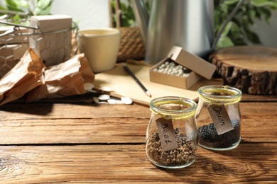 Glass jars with vegetable seeds on wooden table, space for text
