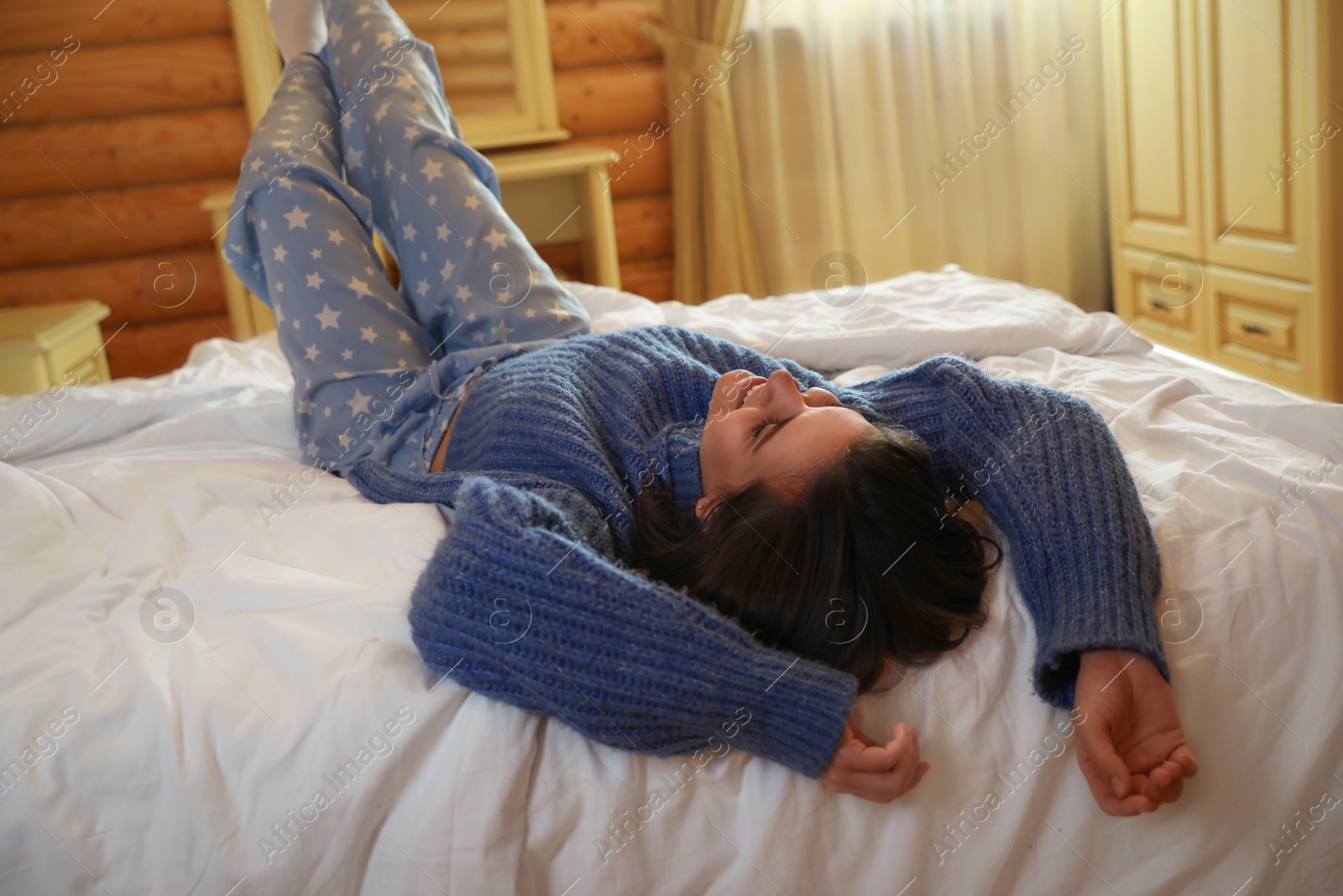 Photo of Young woman wearing warm sweater on bed at home