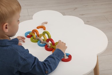 Photo of Motor skills development. Boy playing with colorful wooden arcs at white table. Space for text