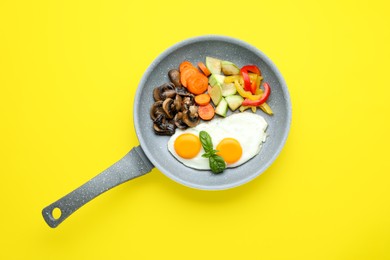 Tasty fried eggs with vegetables in pan on yellow background, top view