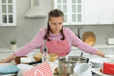 Photo of Upset woman in messy kitchen. Many dirty dishware and utensils on table