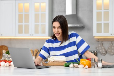 Photo of Young woman cooking while watching online course via laptop in kitchen