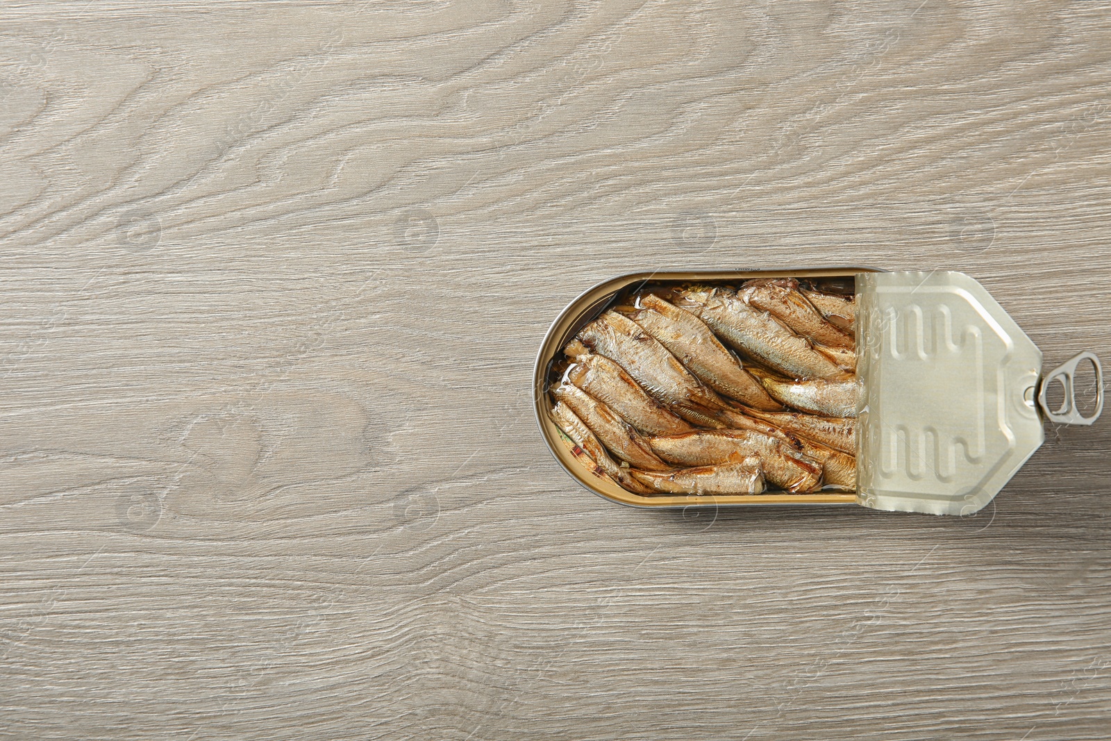 Photo of Open tin can of sprats on wooden background, top view. Space for text