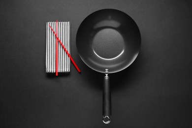Photo of Empty iron wok and chopsticks on black table, flat lay