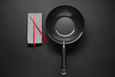 Empty iron wok and chopsticks on black table, flat lay