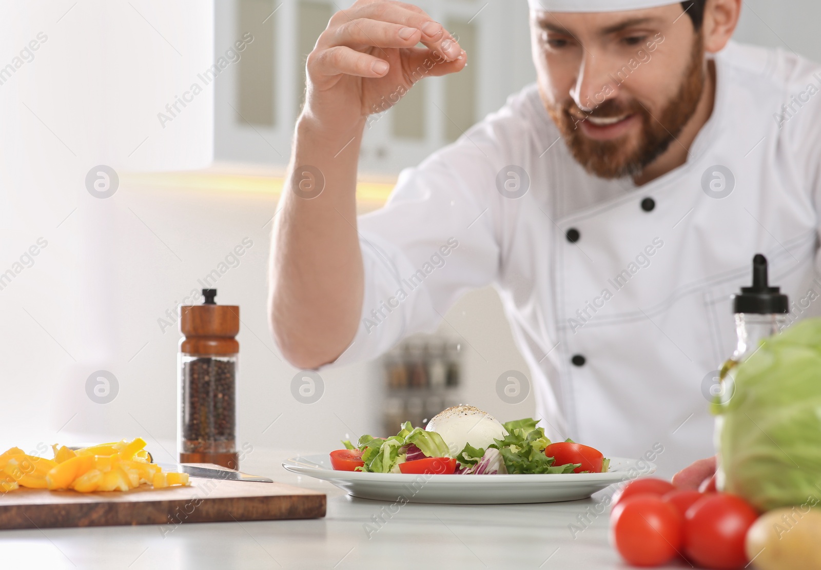 Photo of Professional chef salting delicious salad at marble table, focus on food