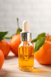 Photo of Bottle of tangerine essential oil and fresh fruits on white wooden table, closeup