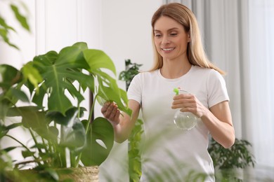 Photo of Woman spraying beautiful houseplants with water at home