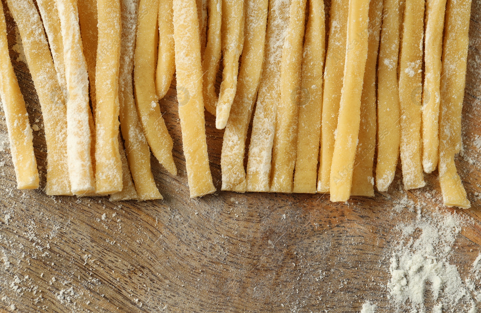 Photo of Raw homemade pasta and flour on wooden table, closeup. Space for text