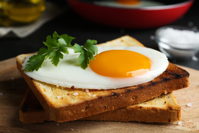 Photo of Tasty fried egg with bread and parsley on wooden board, closeup