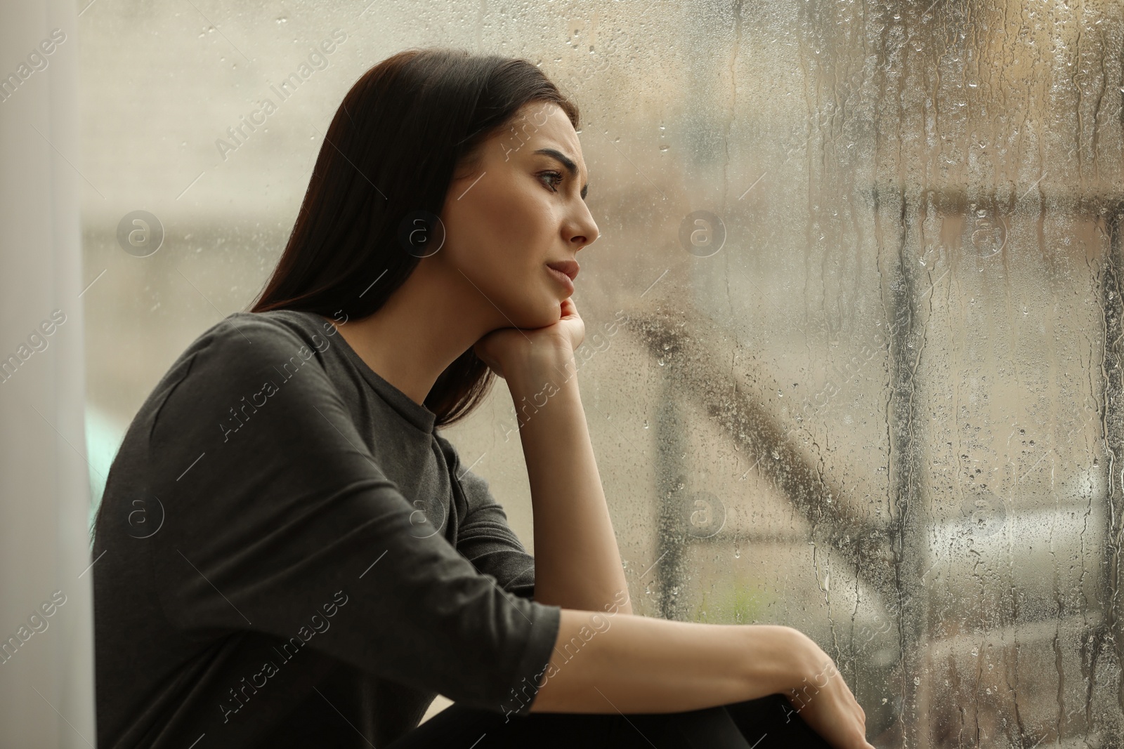 Photo of Depressed woman near window on rainy day, space for text