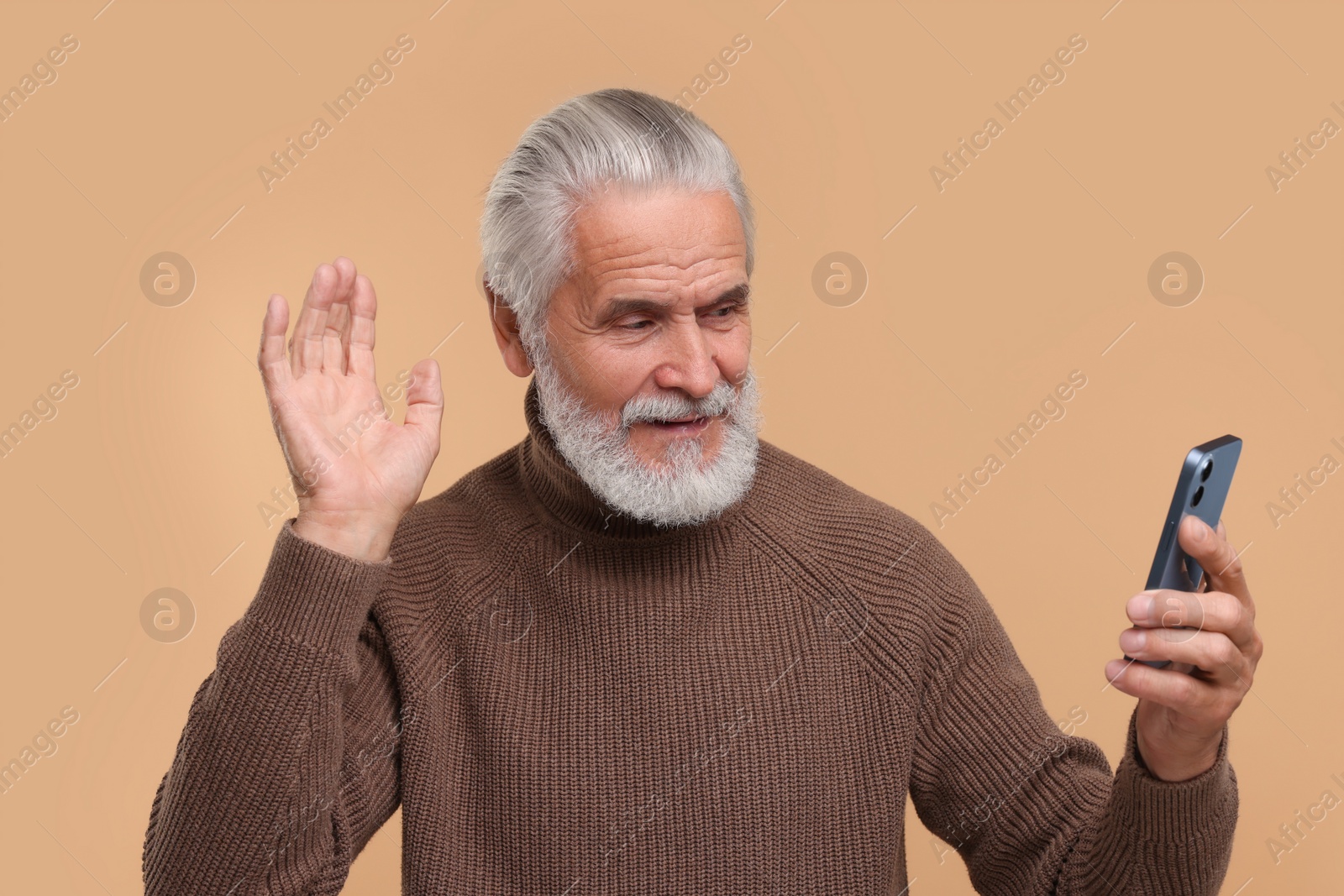 Photo of Senior man with smartphone having video chat on beige background