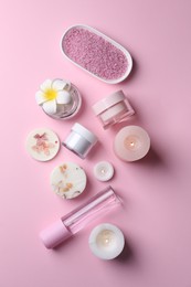 Different spa products, plumeria flower and burning candles on pink background, flat lay