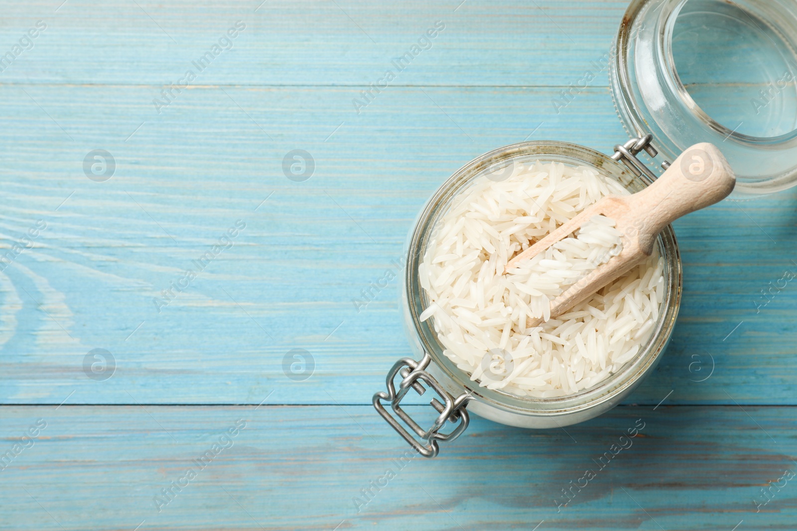 Photo of Raw basmati rice in jar and scoop on light blue wooden table, top view. Space for text