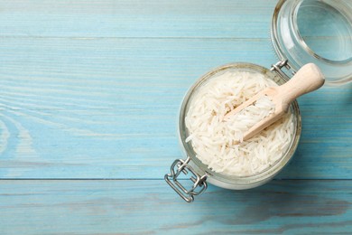 Photo of Raw basmati rice in jar and scoop on light blue wooden table, top view. Space for text