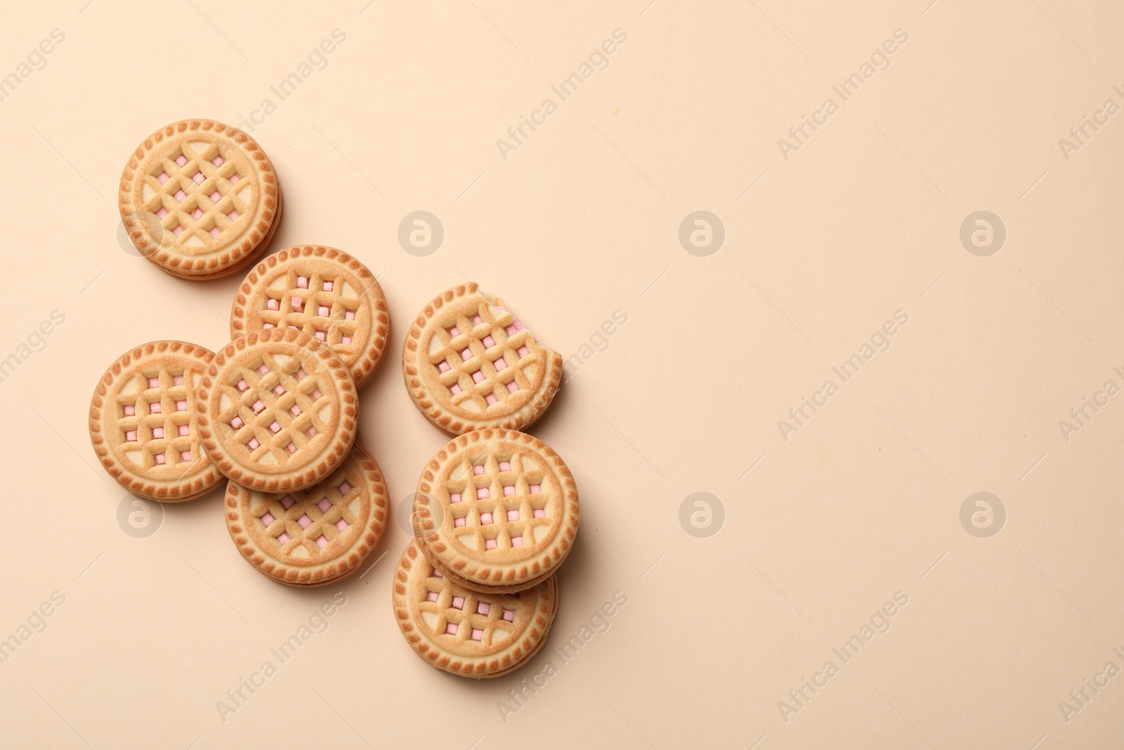 Photo of Tasty sandwich cookies with cream on beige background, flat lay. Space for text