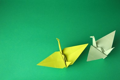 Photo of Colorful paper origami cranes on green background, flat lay. Space for text