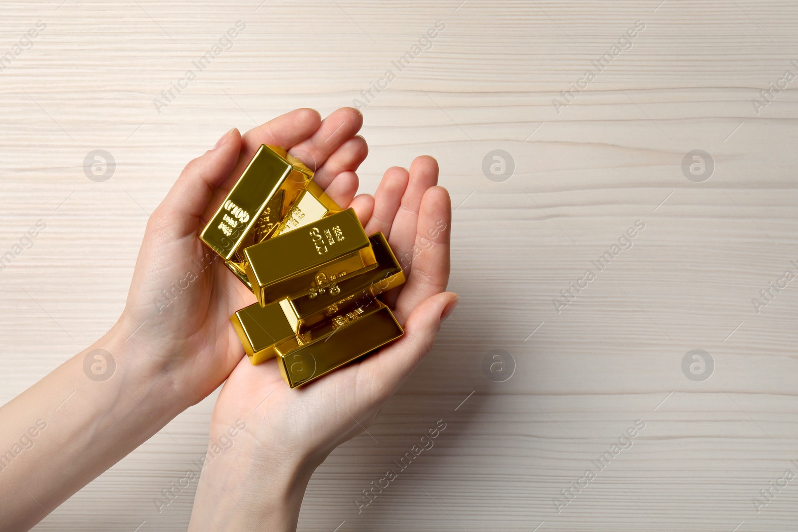 Photo of Woman holding gold bars on white wooden table, top view. Space for text