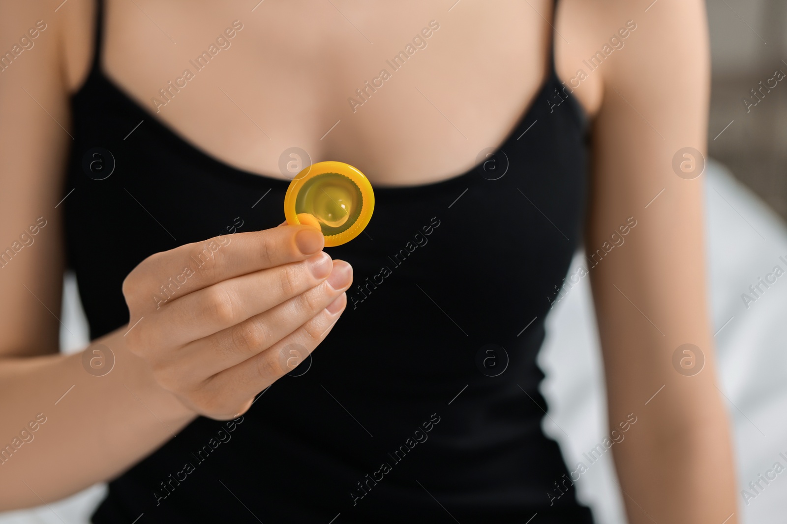 Photo of Woman holding unpacked condom on blurred background, closeup. Safe sex