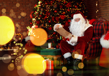 Photo of Santa Claus with wish list near Christmas tree indoors