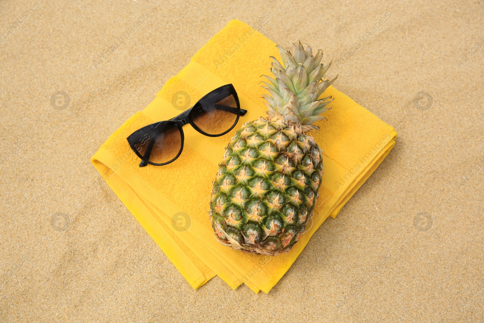 Photo of Fresh pineapple, sunglasses and towel on sand, top view