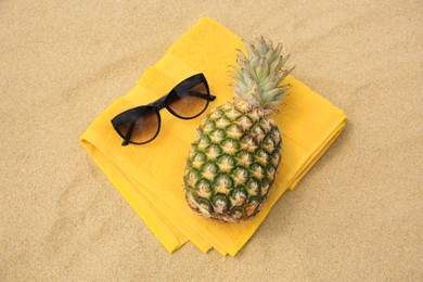 Fresh pineapple, sunglasses and towel on sand, top view