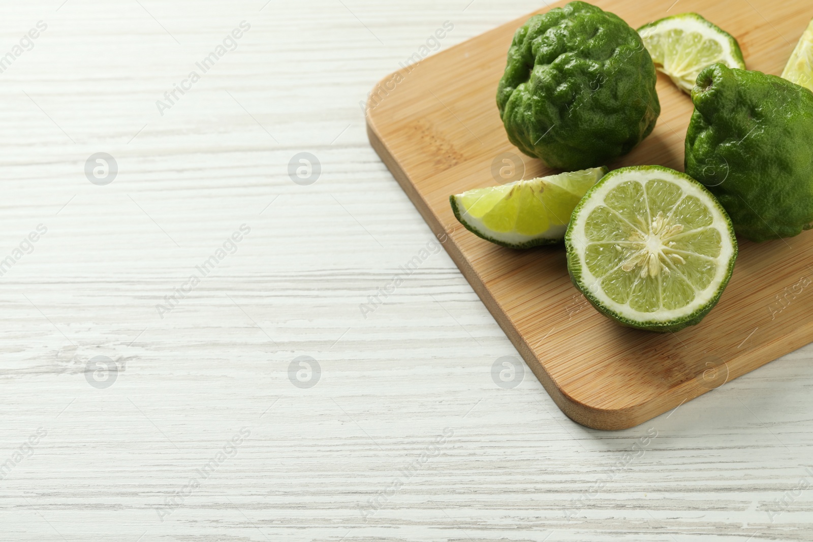 Photo of Whole and cut ripe bergamot fruits on white wooden table, space for text