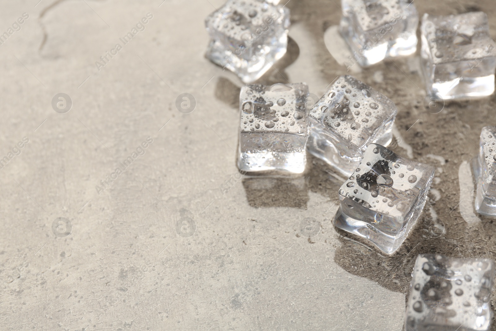 Photo of Melting ice cubes and water drops on grey textured table, closeup. Space for text