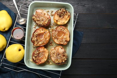 Photo of Tasty baked quinces with nuts and honey in dish on black wooden table, flat lay. Space for text