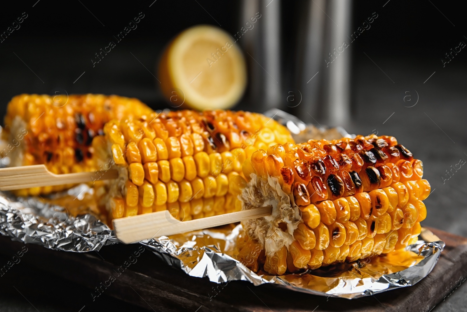 Photo of Foil with delicious grilled corn cobs on table, closeup