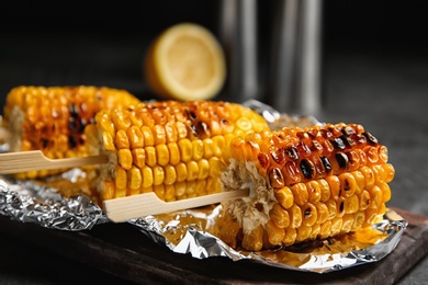 Photo of Foil with delicious grilled corn cobs on table, closeup