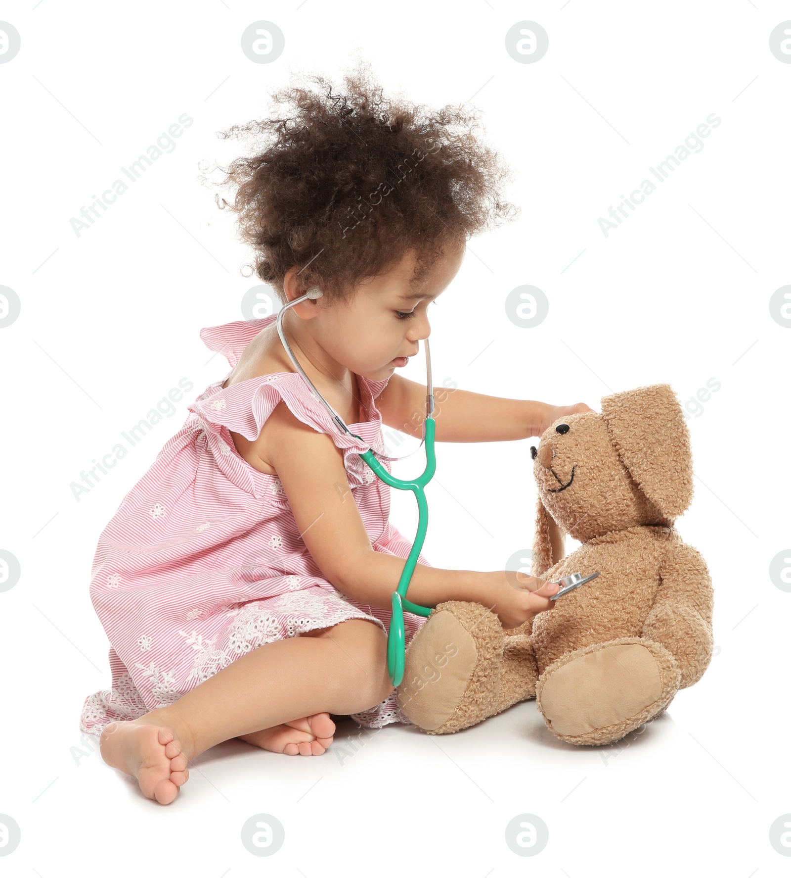 Photo of Cute African American child imagining herself as doctor while playing with stethoscope and toy bunny on white background