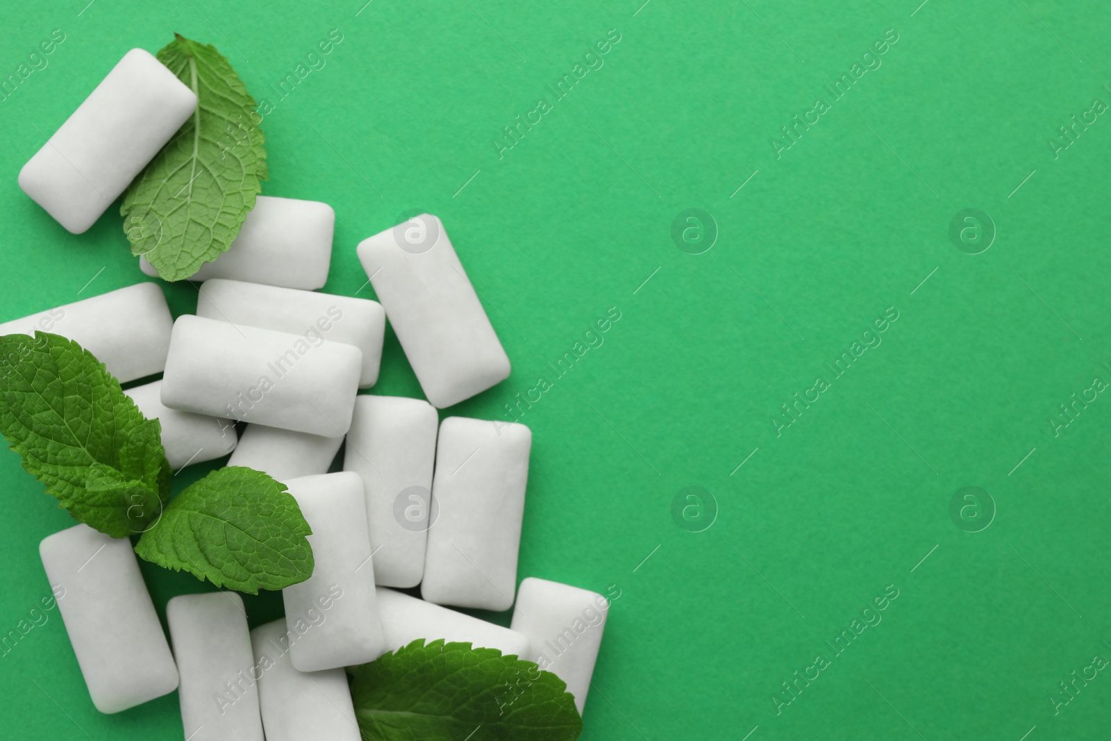 Photo of Tasty white chewing gums and mint leaves on green background, top view. Space for text