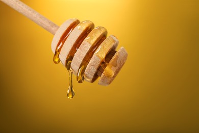 Delicious honey flowing down from dipper against golden background, closeup. Space for text