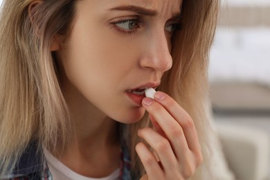 Upset young woman taking abortion pill on blurred background, closeup