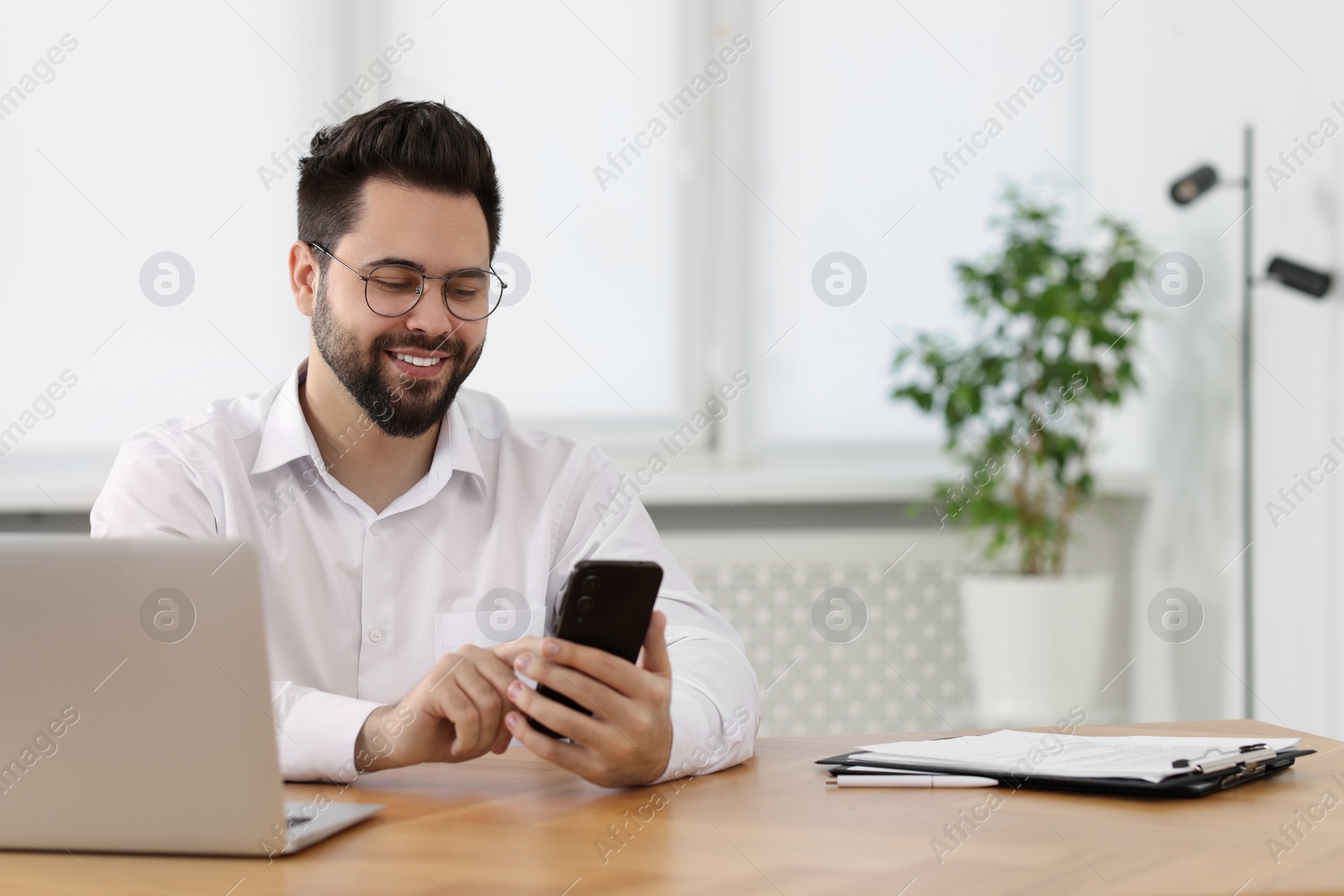 Photo of Handsome young man using smartphone at wooden table in office