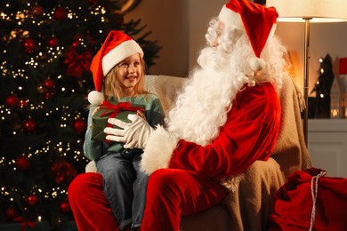 Photo of Merry Christmas. Santa Claus giving gift to little girl in room